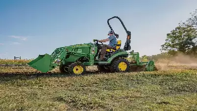 Picture of a landscape contractor on a John Deere tractor with a front loader attachment and a tiller attachment rototilling recently bushhogged land in preperation for planting